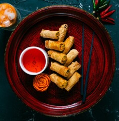 Thai eggrolls with sauce, chopsticks on a red round plate