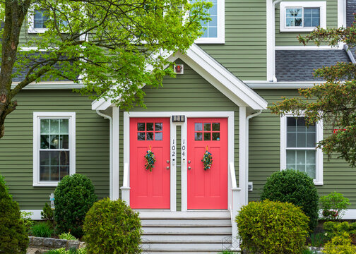 Symmetrical green duplex with coral twin doors framed by spring greenery in Brighton, Massachusetts, USA 
