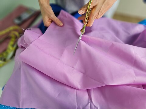 Tailoring process with hands cutting pink fabric using scissors in a creative workshop - Powered by Adobe