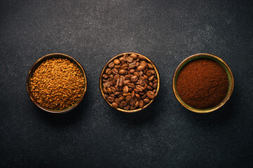 Roasted coffee beans, ground coffee and instant coffee in bowls at dark background.