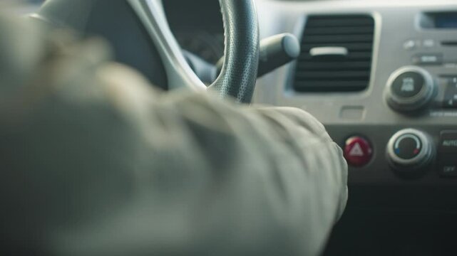 close up hand view of driver removing hand from ignition after turning on car, focus on steering wheel and dashboard area with climate controls and hazard button clearly visible