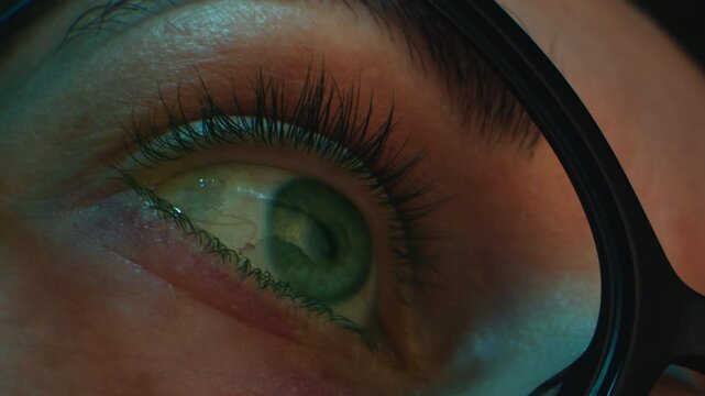 Close up of tired woman working at night on laptop, girl in eye glasses with reflections overworking busy, using computer in dark office