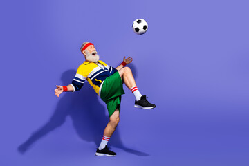 Funny man in retro sportswear practicing football skills with purple background depicting active...