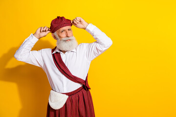 Portrait of a cheerful senior man wearing traditional Scottish attire in a joyful pose against a vibrant yellow background