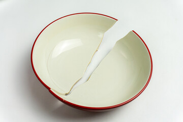 broken soup bowl, likely made of ceramic, with a red rim. It is split diagonally into two pieces. 
