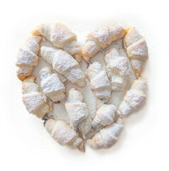 Several croissant-shaped pastries arranged in a heart shape and sprinkled with powdered sugar.