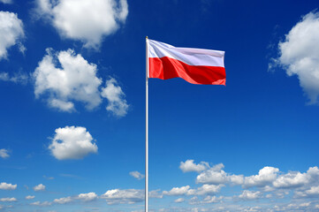 flag of Poland fluttering in the blue sky with cumulus clouds