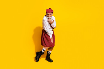 Cheerful elderly man in traditional Scottish attire on yellow background having fun model posing with stylish gestures