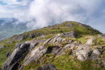 Experience the stunning and breathtaking view of rocky Slieve Foye mountain terrain emerging gracefully through clouds, showcasing vibrant lush greenery and rugged natural beauty, Carlingford, Ireland