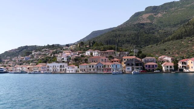 Charming pastel waterfront houses and sailboats along the tranquil blue waters of Vathy Harbor, nestled beneath lush green hills on Ithaca Island, Greece.