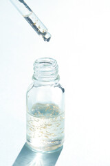 Clear glass bottle with dropper and suspended gold particles on light background.