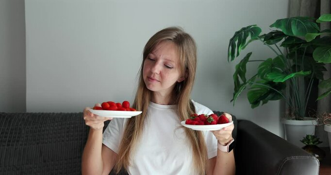 Woman holding plates of strawberries and cherry tomatoes indoors, comparing fresh fruits, healthy diet decision, nutrition concept.