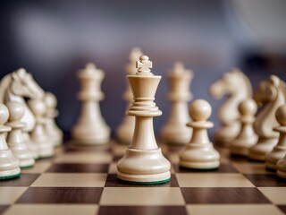 Close-up of a wooden chess king surrounded by various chess pieces on a checkered board.