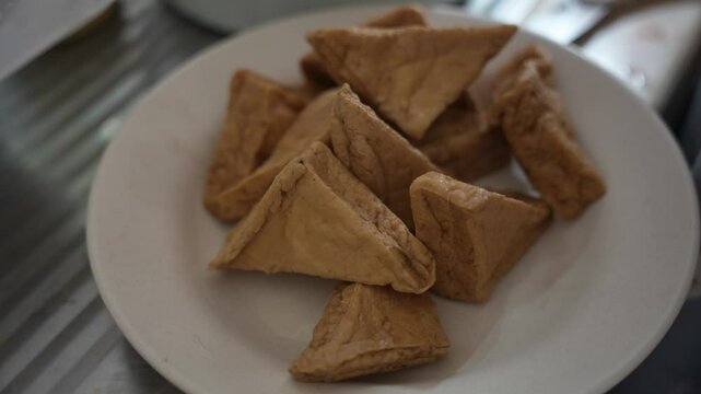 Triangular fried tofu on a white plate in the kitchen.