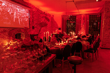 Red Velvet Banquet Room.
Luxurious dining room glowing in red lighting, with elegantly set tables, candles, floral decor, and stone walls — perfect for an exclusive masquerade or themed celebration.