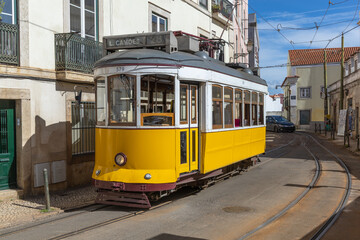 A classic yellow Tram 28 navigates the charming, narrow streets of Lisbon, Portugal on a sunny day.