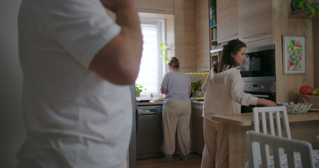 Obraz premium Group of people standing in modern kitchen preparing food together, casual family setting, focus on woman in hoodie, warm atmosphere of shared cooking moments