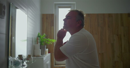 Man shaving close-up, razor gliding under neck, focusing on clean shave, bathroom background with natural wooden details, precise grooming moment, calm atmosphere