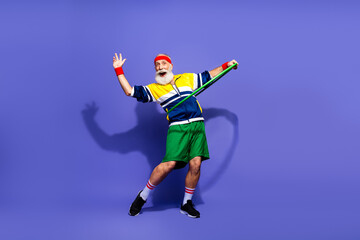 Cheerful man in vibrant retro activewear exercising with a resistance band against a purple backdrop, showing fitness and humor