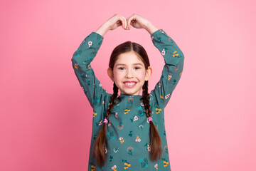 Smiling young girl in casual clothing expressing joy with hand gesture against pink background
