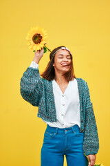Woman holding sunflower and smiling with eyes closed on yellow background