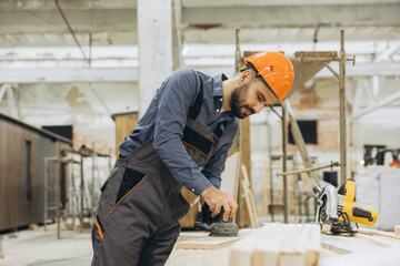 Carpenter sanding wooden plank in modular building factory