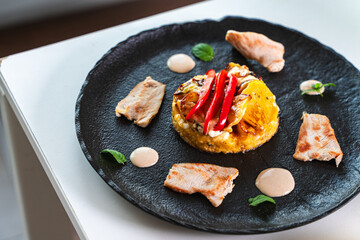 Slices of cooked turkey with potato tortilla and red bell peppers on a black plate with sauce. Beautiful presentation of dinner.