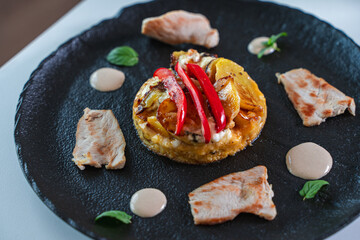 Slices of cooked turkey with potato tortilla and red bell peppers on a black plate with sauce. Beautiful presentation of dinner.