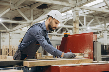 Fototapeta premium Carpenter measuring wooden plank in modular building factory