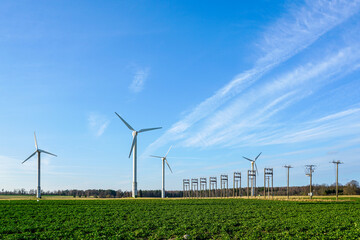 Tall wind turbines with power transmission line generating renewable energy amidst green fields