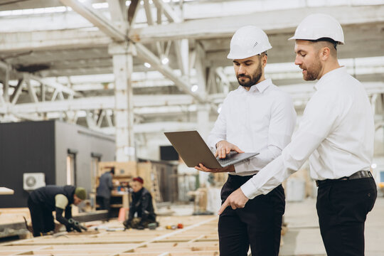 Engineers using laptop are supervising construction workers building modular house