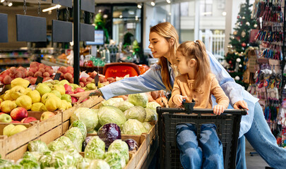 Mother and daughter choosing fresh fruits and vegetables in grocery store
