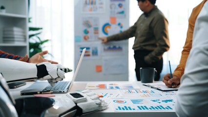 A modern workspace featuring a robotic arm assisting in data analysis, illustrating teamwork and innovation in a business environment with charts and graphs.Noogenesis