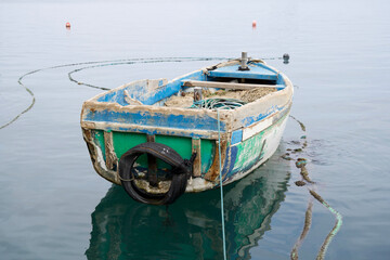 Obraz premium Weathered fishing boat floating on calm water, surrounded by gentle ripples and reflections, showcasing rustic charm and tranquility in a serene marine environment with soft colors