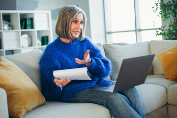 Mature woman relaxing at home, using laptop for remote work or communication, embracing comfort and...