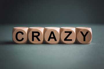 Wooden cubes spelling word crazy on dark background, showcasing a concept of unpredictability or excitement