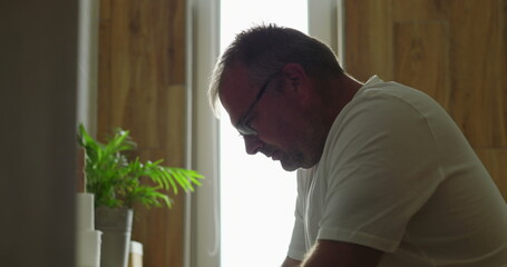 Man in profile view in front of bathroom mirror with gentle expression, reflecting indoors, light...