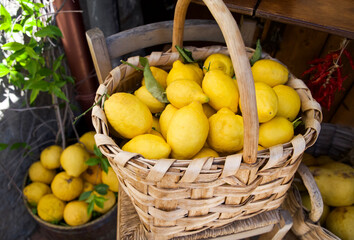 Freshly harvested lemons in a woven basket, surrounded by greenery and rustic wooden elements,...