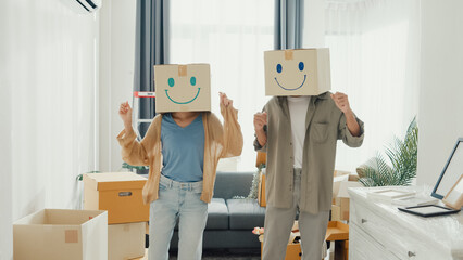 Happy Asia couple stand front of sofa couch used carton box made smiling face funny dance front of camera together in living room at new house. Husband and wife moving new house, Couple goal Concept.