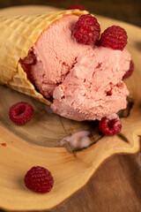 pink ice cream lies on a walnut board close up, ripe red raspberries and raspberry cold natural ice cream on the table