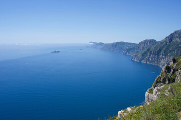 Italian expansive coastal view showcasing serene blue ocean meeting rugged cliffs under clear sky, with distant islands visible on the horizon, creating a tranquil and picturesque natural landscape
