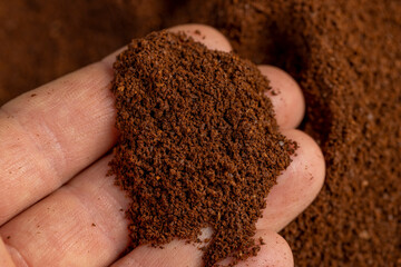 Coffee in hand, ground coffee beans for preparation of a drink, roasted ground coffee in large quantities