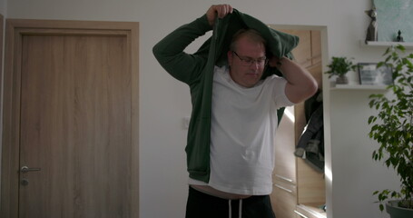 Man putting on jacket indoors, getting ready for the day, standing near door in home environment,...