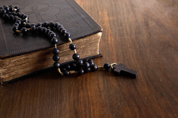 Vintage Holy Bible with lots of ornaments on the cover and old rosary on vintage wooden desk....