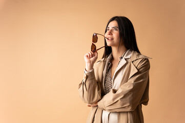 Stylish woman holding sunglasses and looking up on beige background