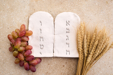 Happy Shavuot concept. Two Stones with Ten Commandments in Ancient Hebrew, Grains, milk and cheese
