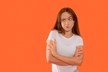 Obraz premium Young woman expresses confusion while standing against a vibrant orange background in a casual white t-shirt