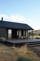 Modern rural house with wooden deck set against a scenic backdrop of rolling hills and clear blue sky during the golden hour in the countryside