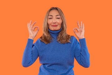 Meditation practice by a woman in a blue sweater against an orange background in a calming indoor...