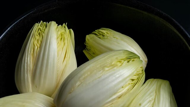 Endive heads nestled inside a dark bowl, ready to be used in a salad or other culinary creation with fresh green details.